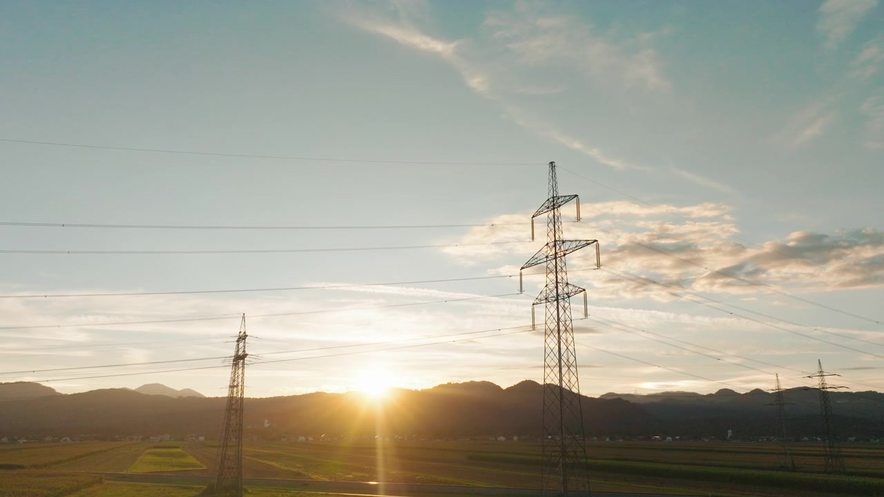 Power lines and towers are visible in a rural area as the sun sets in the background highlighting