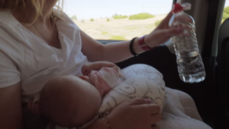 woman drinking water during breastfeeding in the car