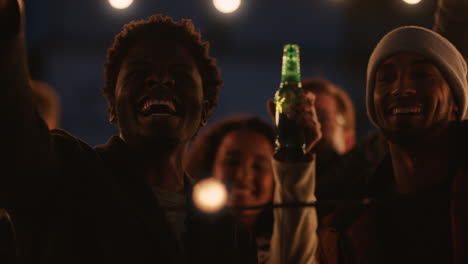 happy rooftop party friends having fun young african american man taking photos using smartphone sharing weekend lifestyle on social media at night