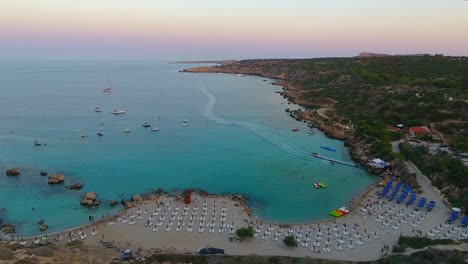 Vistas-De-Drones-De-La-Mundialmente-Famosa-Playa-De-Konnos-En-La-Isla-Mediterránea-De-Chipre-A-última-Hora-De-La-Tarde-Después-Del-Atardecer-Con-Agua-De-Mar-Turquesa-Clara