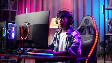 un adolescente asiático serio jugando videojuegos en la computadora.