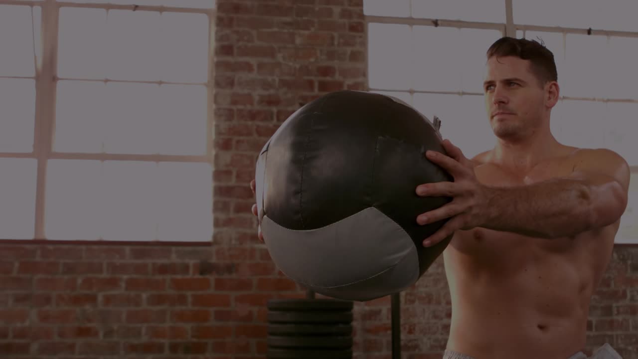 From forward hold man shifting grip, rotating med ball, showing core while finance charts drifting