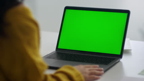 Back-view-unrecognized-woman-looking-green-screen-laptop-computer-in-office.