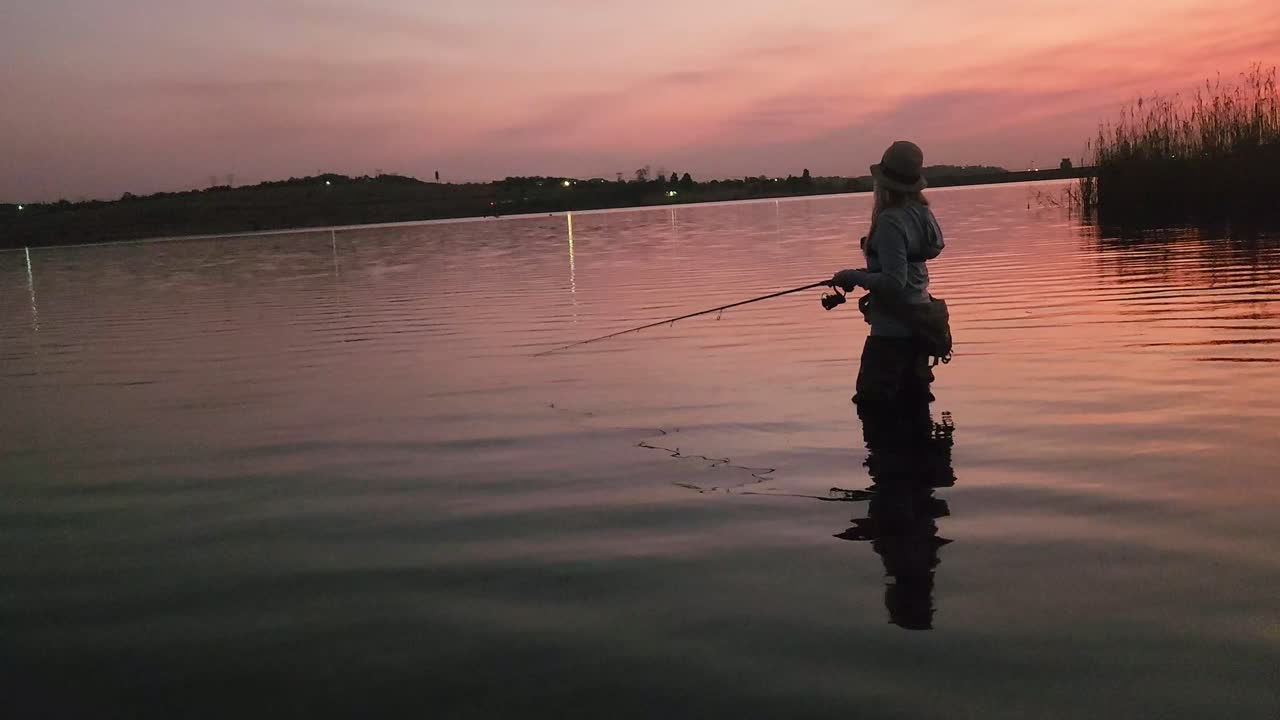 Seorang wanita memancing di danau yang indah dan tenang tepat setelah senja merah muda