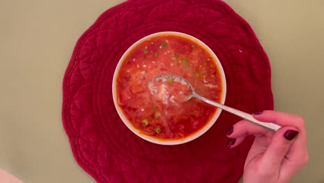 hand stirring sour cream into vibrant red borscht soup.