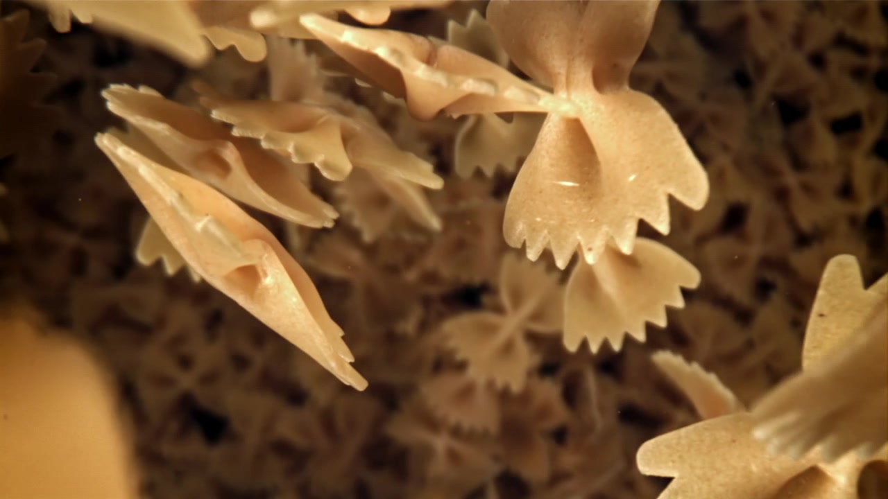 Pasta farfalle cruda che galleggia e affonda nell'acqua