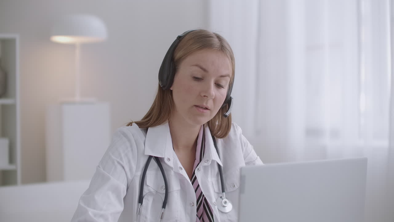una joven médica se está comunicando con el paciente en línea por computadora portátil utilizando videollamada y auriculares con micrófono