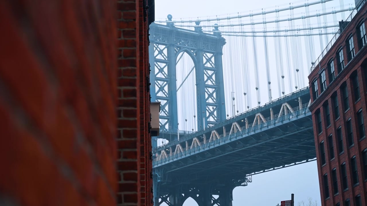 2025年12月25日、アメリカ、ニューヨーク：ブルックリンのダンボ地区にある、ぼやけたレンガ壁とマンハッタン橋の構造。霧の中、赤いレンガの建物に縁取られたマンハッタン橋の鉄骨塔の詳細な景色。