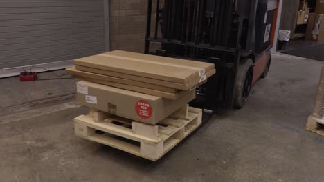 electric fork lift moving pallet and boxes forward then lifting them out of frame