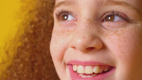 close up studio portrait of smiling girl with red hair against yellow background