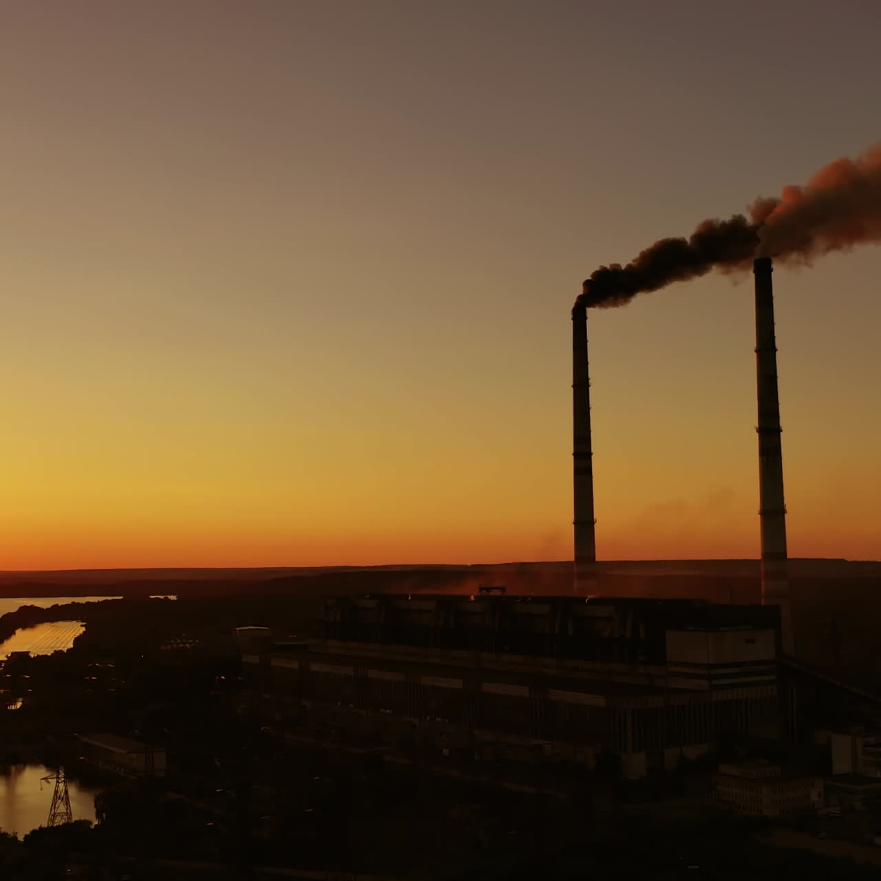 Harmful emissions from factory at sunset. Dangerous smoke goes in the air from industrial plant near the river. Ecological disaster.