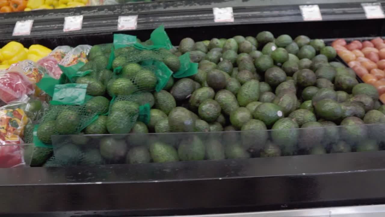 Fresh produce display of avocados, tomatoes, and limes in a grocery store aisle