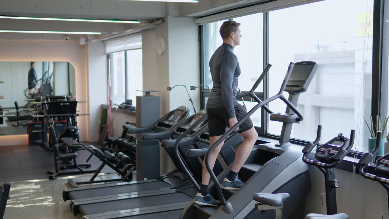 Man athlete in 30s using stair climbing machine to burn calories in empty gym