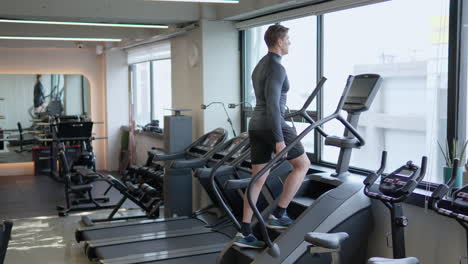 man athlete in 30s using stair climbing machine to burn calories in empty gym