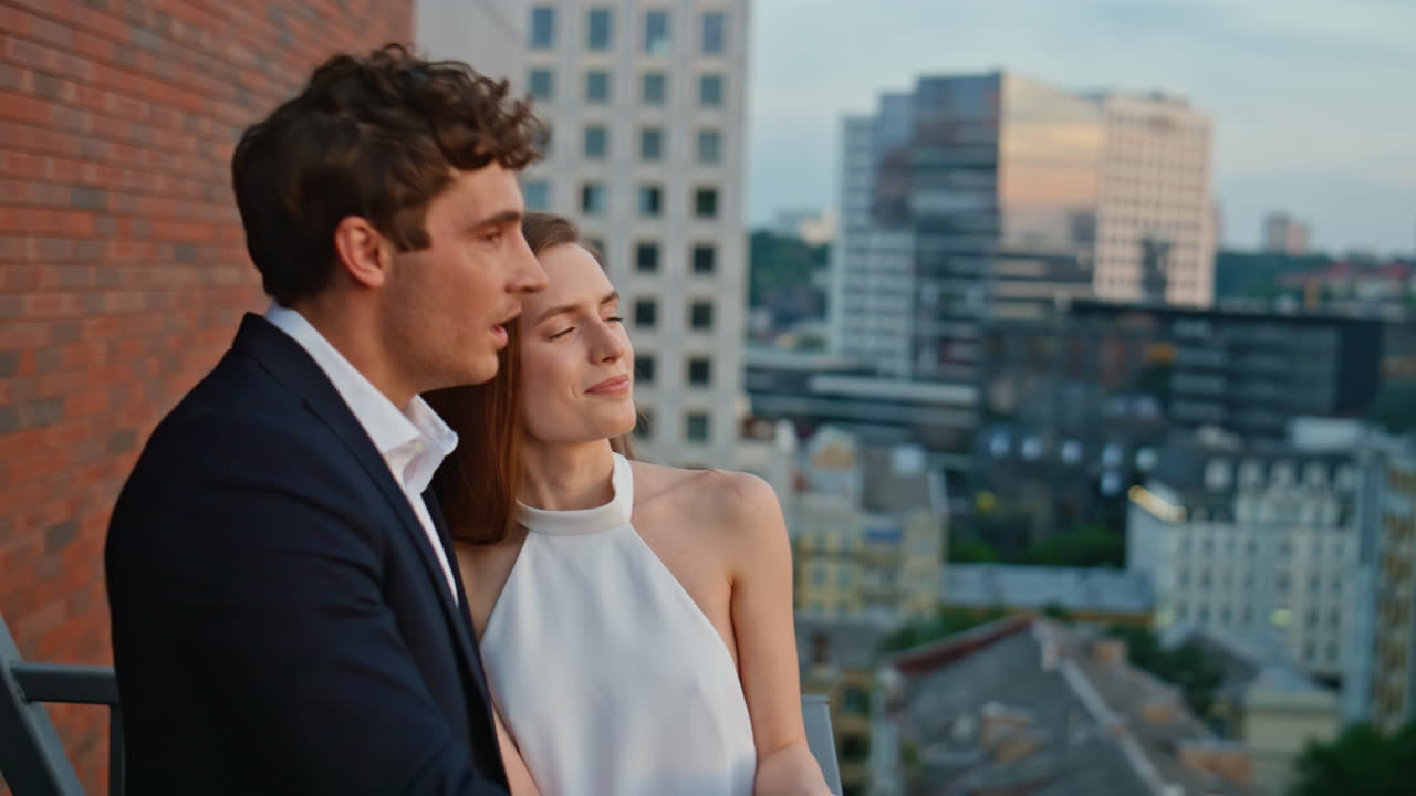 Laughing pair looking city view standing on balcony in luxury outfit closeup