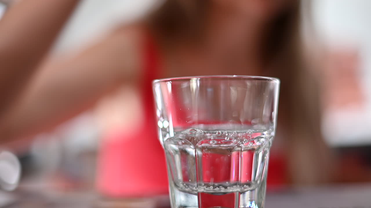 Nainen punaisessa mekossa kaatamassa vettä lasiin ravintolassa