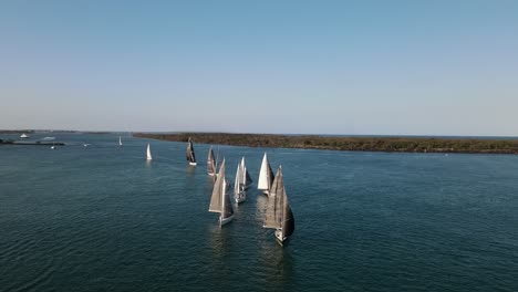 high panoramic drone view moving towards a group of sailing boats racing along the water in the afternoon sunset light