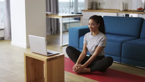 Young-African-woman-doing-stretching,-warming-up-her-joints-in-front-laptop