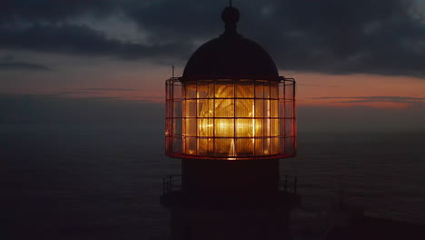 Close-up-of-lighthouse-shining-head-fresnel-lens-at-dusk,-drone-circling-around-reveals-sensational-evening-sea-panorama,-Lagos,-Portugal