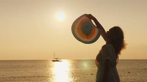 una mujer agita su sombrero hacia un barco distante parado en el muelle temprano en la mañana se encuentra con el amanecer 4k