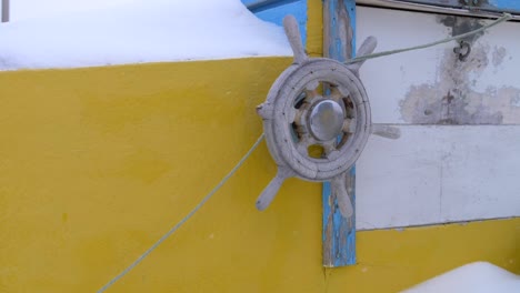 wooden, weathered steering wheel on a yellow boat in a snowstorm in greenland