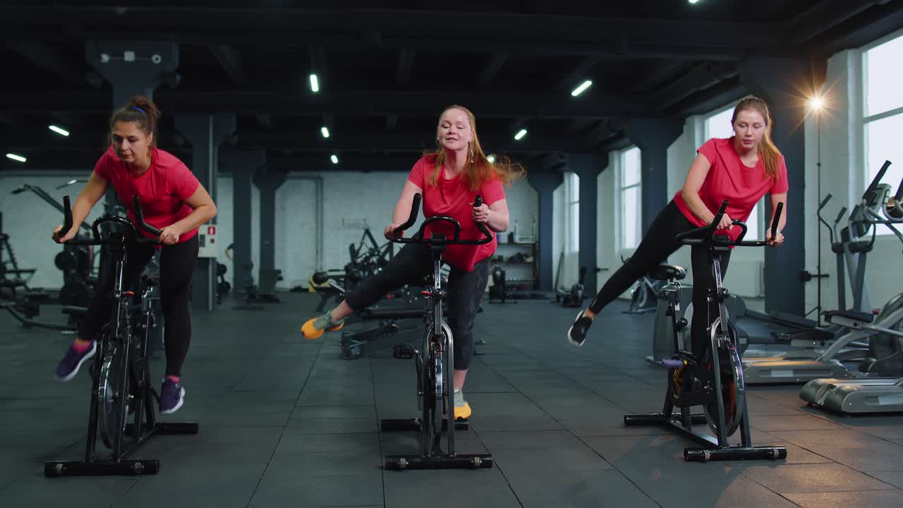 Athletic women group riding on spinning stationary bike training routine in gym weight loss indoors