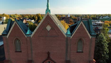 Historic-typical-brick-church,-slate-roof,-crucifix-in-downtown-Lancaster-PA-USA-during-autumn,-fall-foliage-during-dramatic-magic-hour-light,-aerial-drone-view