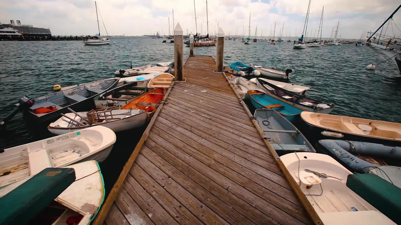 Små fiskerbåde bundet til en træmole, der vugger i blåt havvand i San Diego havn