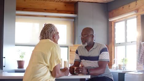 happy senior african american couple drinking coffee and talking in kitchen, slow motion