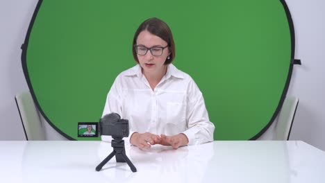 young woman wearing glasses records entertaining or educational video using action camera against background of chromakey. tv presenter is preparing emergency news release in studio