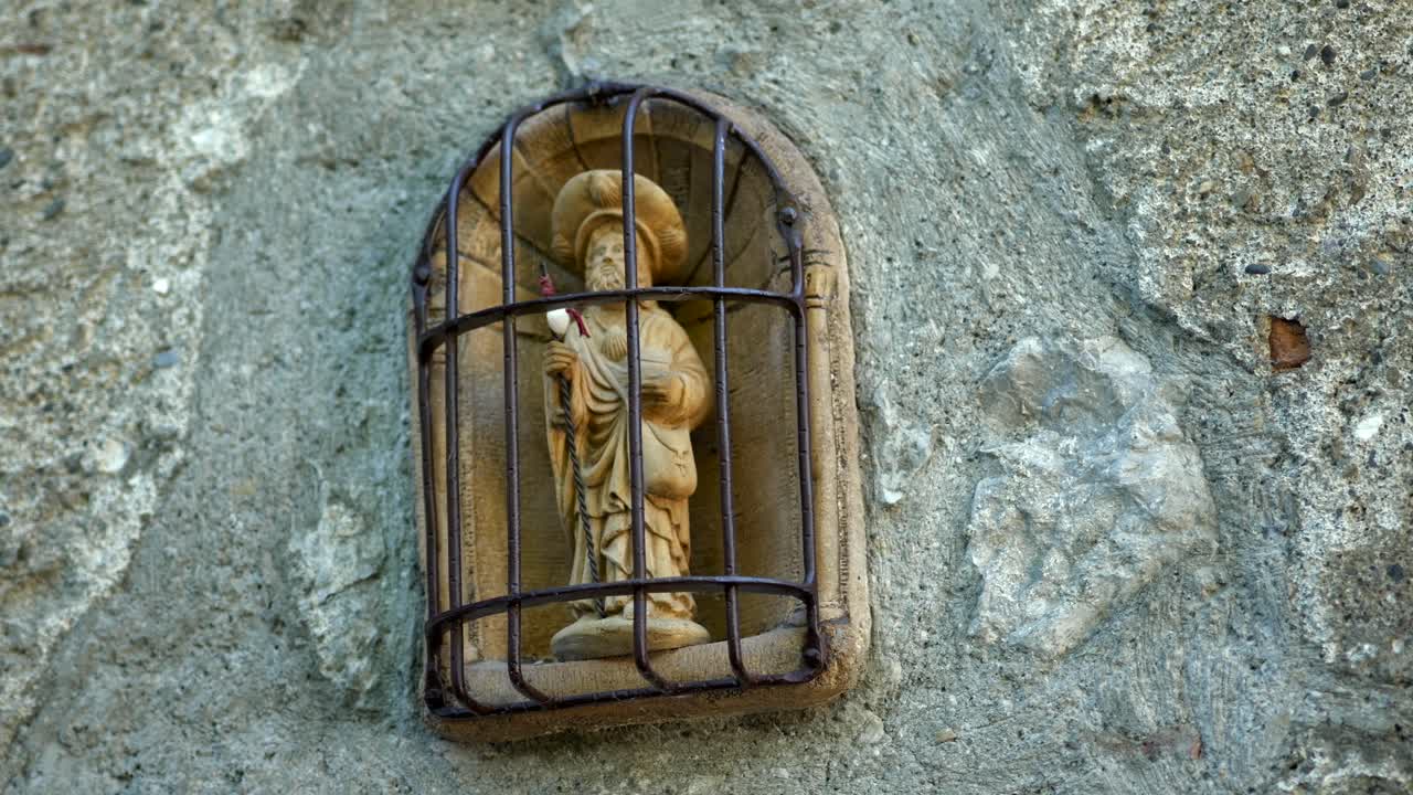 Close up on a small statue of a pilgrim on his way to Santiago with his pilgrim stick and a scallop shell around the neck. Located in the village of Saint-Bertrand-de-Comminges.