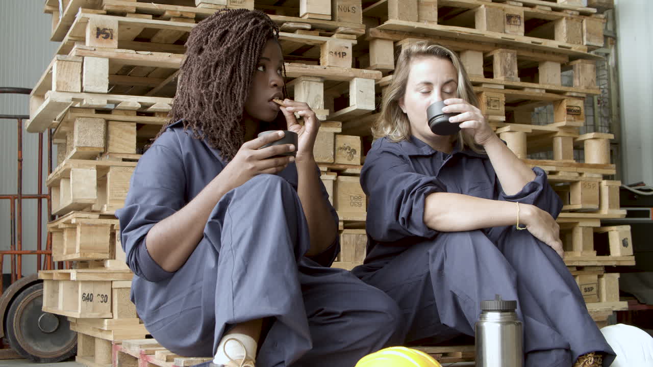 разнообразные рабочие разговаривают, пьют кофе и едят печенье, сидя на деревянном помосте