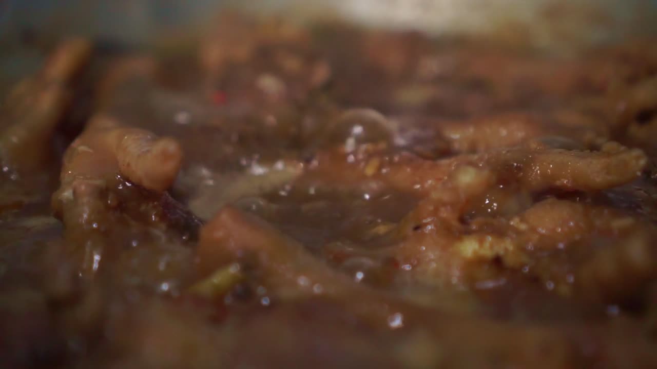 Primo piano di carne di pollo che sobbolle in una ricca salsa bollente. Cucina tradizionale in stile asiatico con sugo bollente e spezie aromatiche in una padella calda.