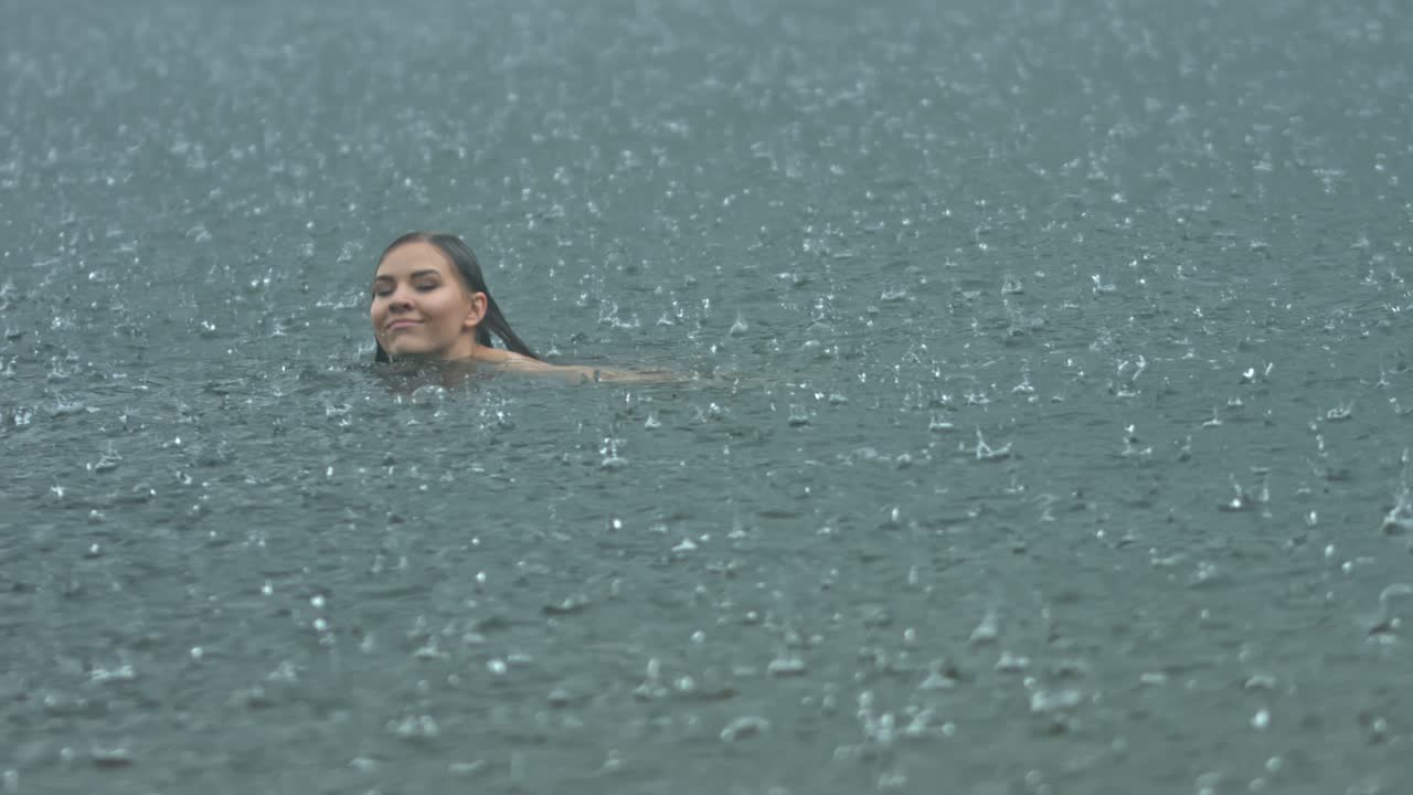 비 기후에서 열린 물에서 밖에서 수영하는 자유를 표현하는 젊은 여성