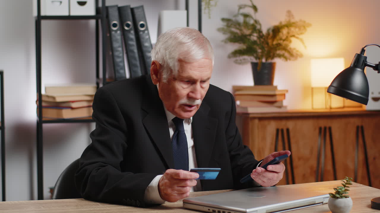 Hvid vred senior forretningsmand forsøger at betale online med smartphone blokeret kreditkort derhjemme