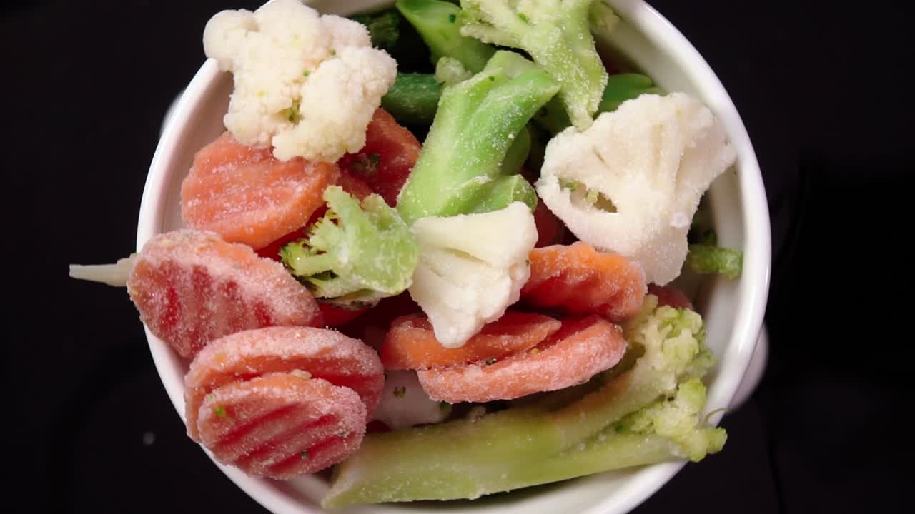 Primo piano di un mix di verdure surgelate, tra cui carote, broccoli e cavolfiore, all'interno di una ciotola su sfondo scuro