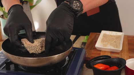 professional chef placing a piece of salmon fillet coated with white sesame into a frying pan with shallow of oil, cooking class concept shot