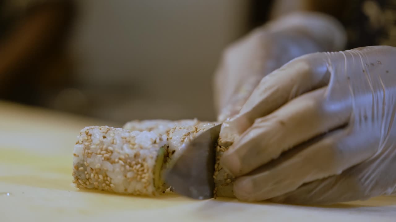 persona con guantes cortando rollos de sushi en rodajas, preparación casera
