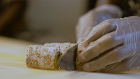 person wearing gloves cutting sushi roll in slices, homemade preparation