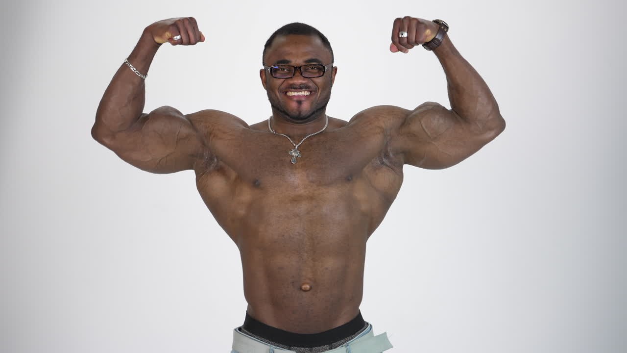 Portrait of athletic african man. Smiling shirtless sportsman with black skin with stretched his arms to the sides and showing his large muscles on white background.