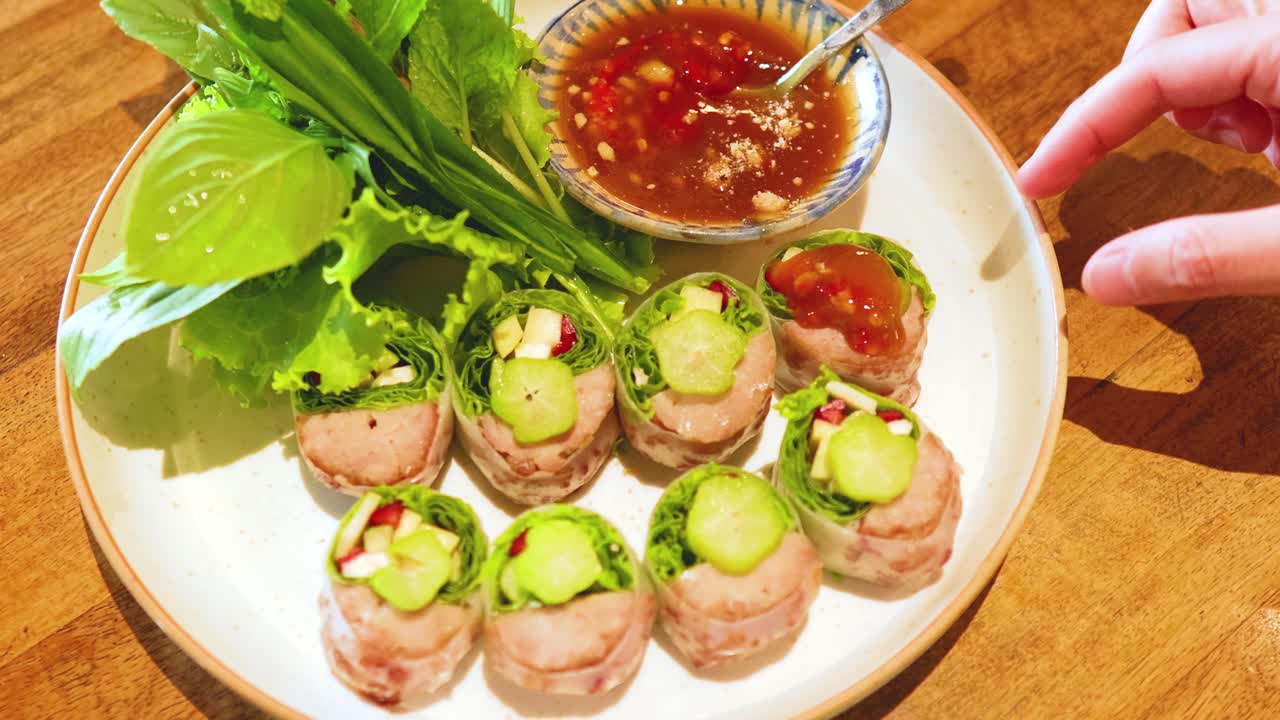 A hand drizzles sauce over Vietnamese pork rolls, highlighting fresh ingredients and vibrant colors in a well-lit setting