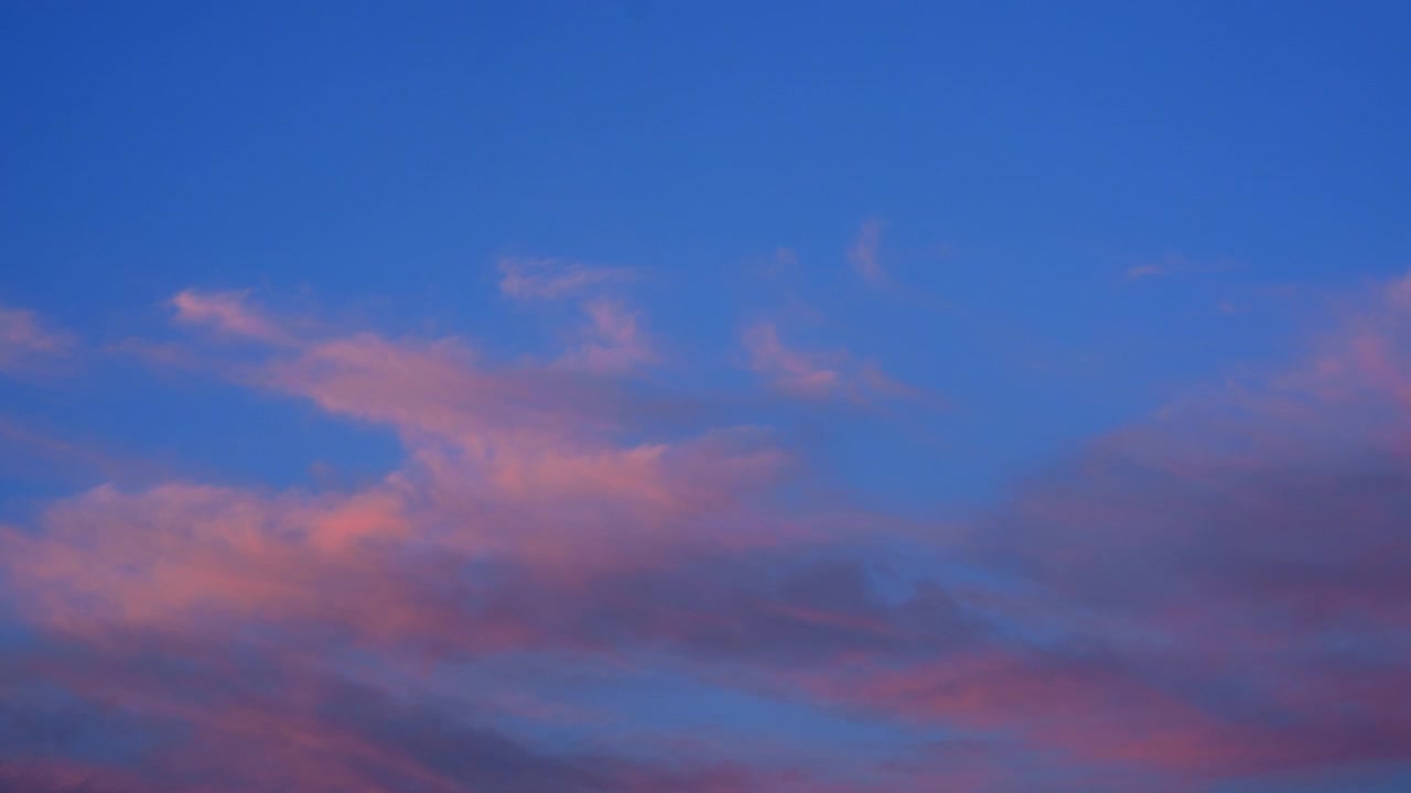 Nuvole rosa e blu tenui che si diffondono nel cielo serale sopra edifici urbani e antenne di comunicazione.