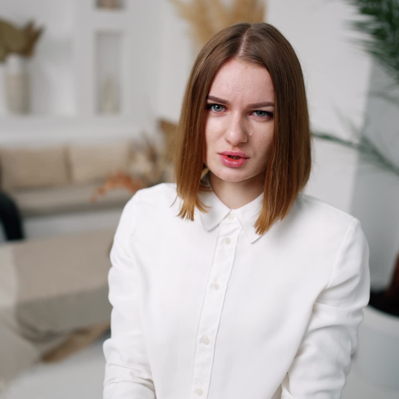 Worried confused concerned young woman looks and points at camera. Close up. Blurred backdrop