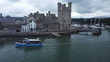 sightseeing boat sailing caernarfon castle welsh harbour town river aerial view tracking left