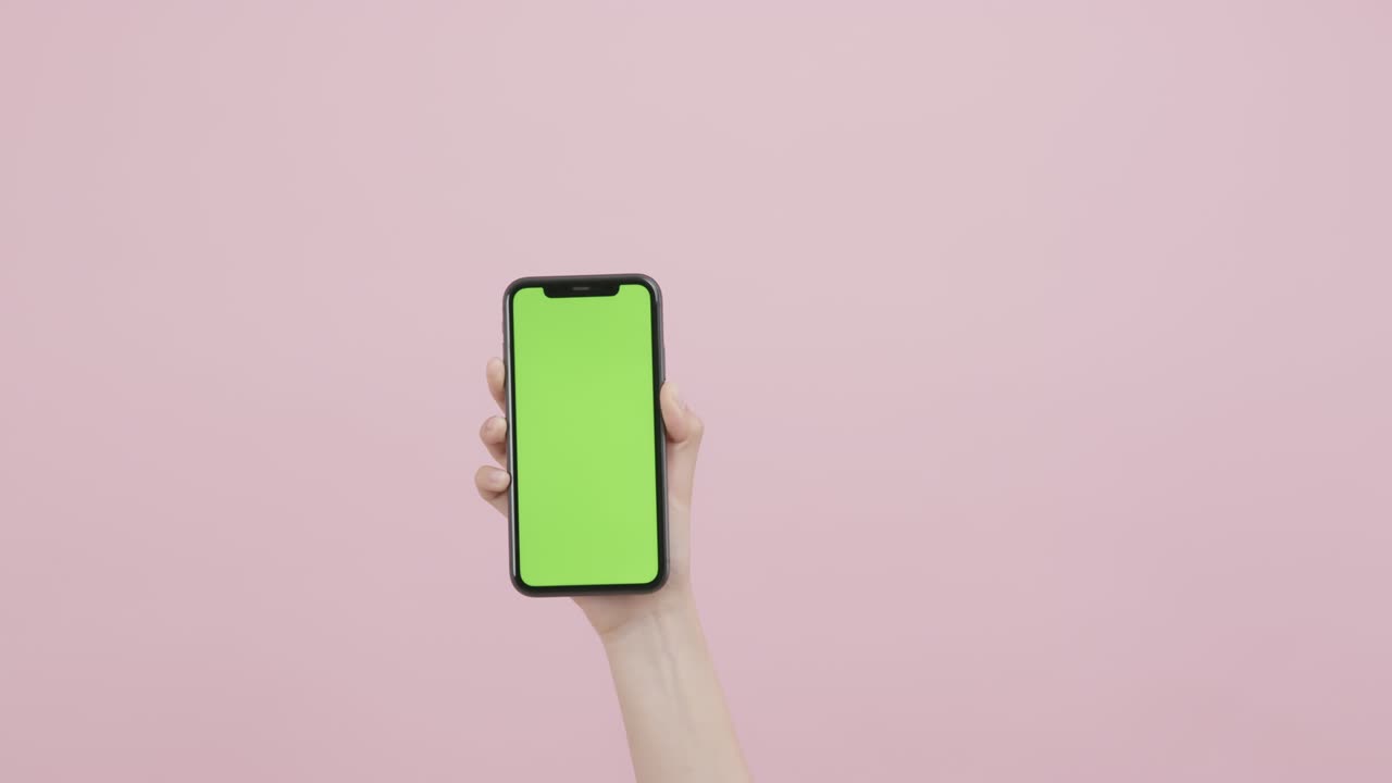 mano sosteniendo un teléfono inteligente con pantalla de tecla de croma y mostrando en el fondo rosa.