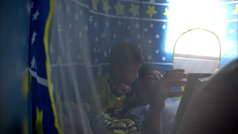 mexican latin brunette mother reading a book to her son laying inside his castle tent having a moment together