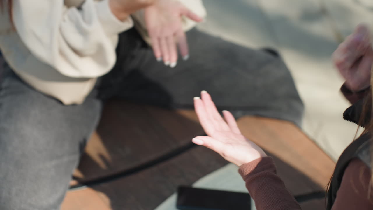 야외 테이블에서 손짓으로 토론하는 두 친구, 벤치에 앉아 책과 휴대폰을 사이에 두고 의견을 주고받는 백인 여성들, 캠퍼스 햇빛, 표현력 풍부한 대화와 경청