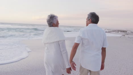 Rückansicht-Eines-Glücklichen-Hispanischen,-Frisch-Verheirateten-älteren-Paares,-Das-Bei-Sonnenuntergang-Am-Strand-Spaziert