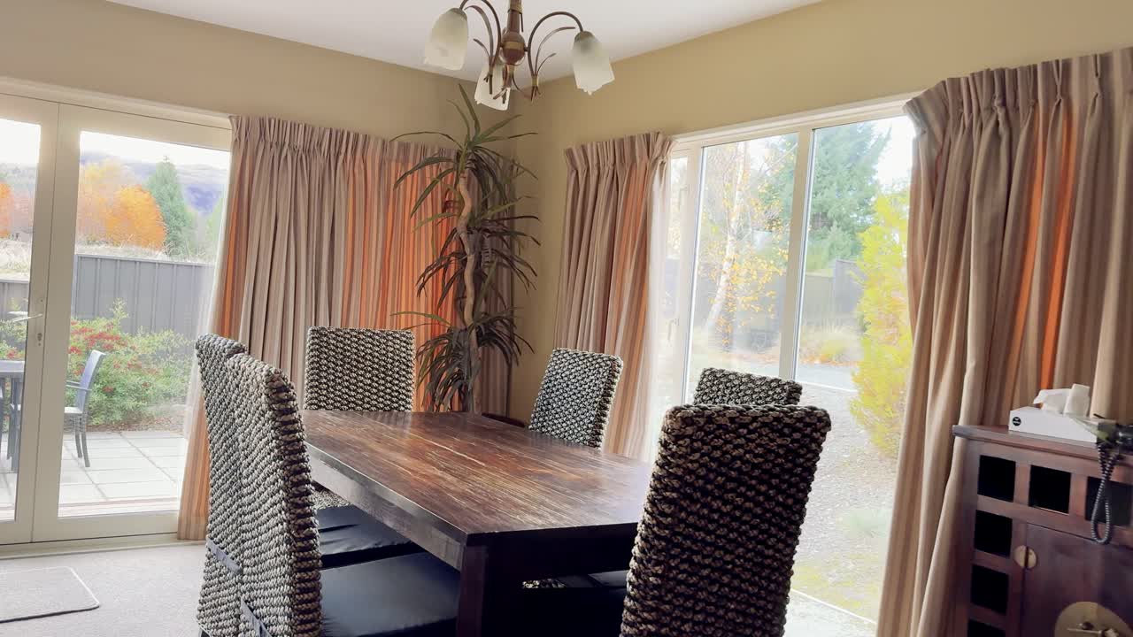 Camera moves through a bright, modern living room and kitchen, revealing large windows, dining area, and outdoor garden in natural daylight