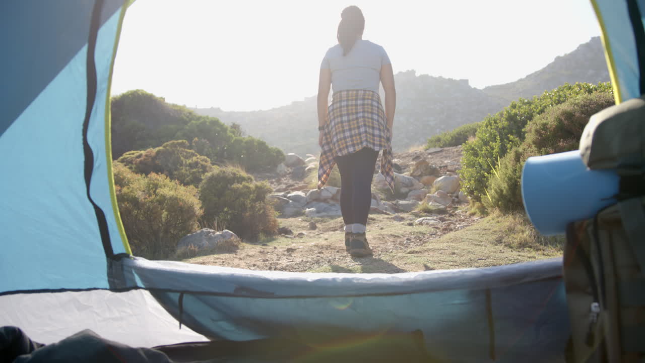 Hiking on mountain trail, woman walking away from tent in morning light